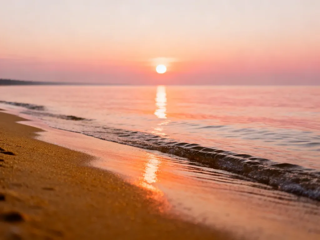 Spokojny wschód słońca nad Bałtykiem w Jantarze, z ciepłymi odcieniami nieba odbijającymi się w wodzie i piaszczystej plaży.